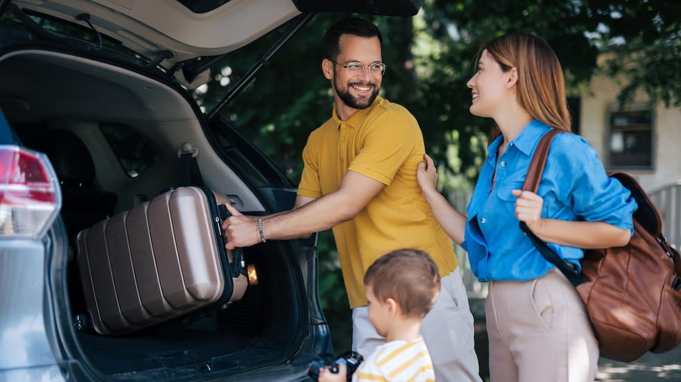 A family joyfully engages in packing their car trunk with luggage for a vacation trip
